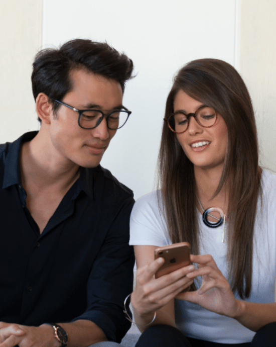 Bărbat și femeie purtând lentile Essilor cu Eyezen în timp ce se uită pe smart phone